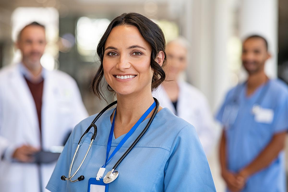 happy nurse in scrubs with other nurses and doctors in the background
